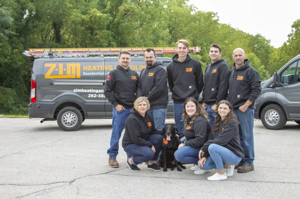 The ZIM Heating & Cooling staff posing in gray-colored company apparel in front of matching work van