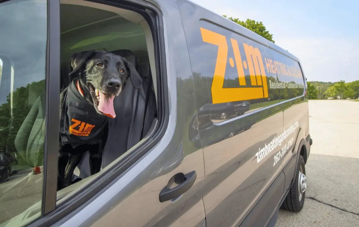 Black lab in driver's seat of a gray and orange work van with ZIM Heating & Cooling - Waukesha HVAC Contractor written on side.