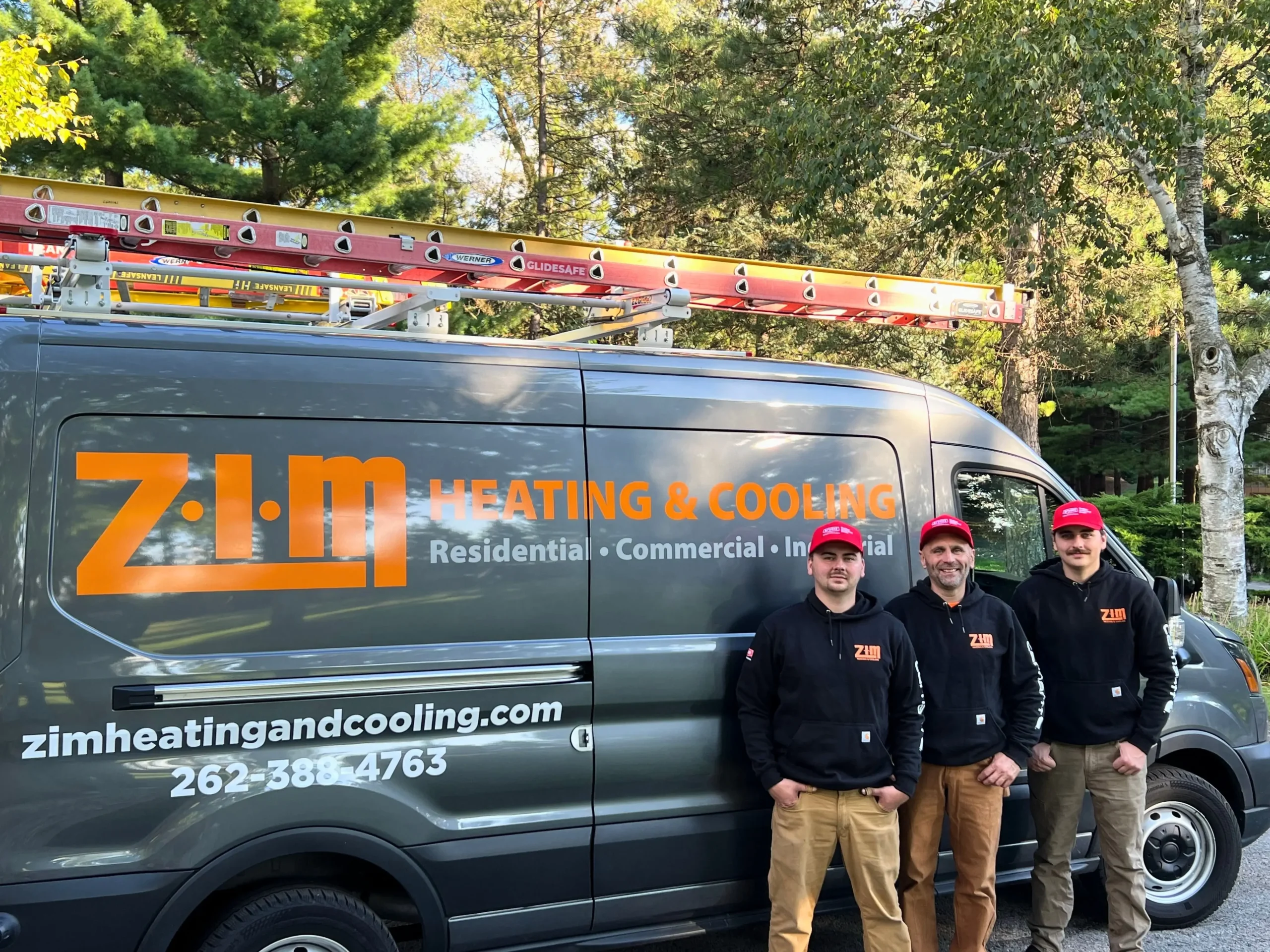 Three ZIM Heating & Cooling HVAC technicians standing in company uniforms in front of company van in Waukesha, WI